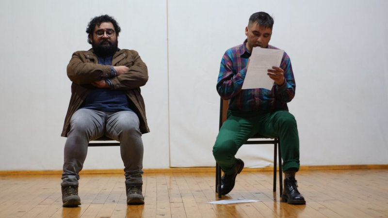 Dos personas sentadas en sillas sobre, una lee un papel